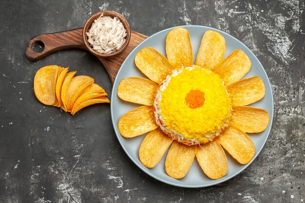 Bovenaanzicht van salade op plaat staan met kom kaas en chips aan kant op donkergrijze achtergrond