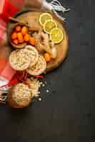 Gratis foto bovenaanzicht van samenstelling met maïsdieet brood kumquats kaneelstokjes citroen plakjes en gember op een houten bord op zwart
