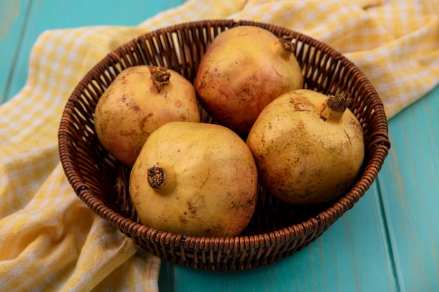 Bovenaanzicht van sappige granaatappels op een emmer op een geel geruit doek op een blauwe houten ondergrond