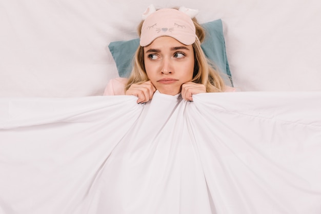 Bovenaanzicht van schattige jonge vrouw liggend onder een deken