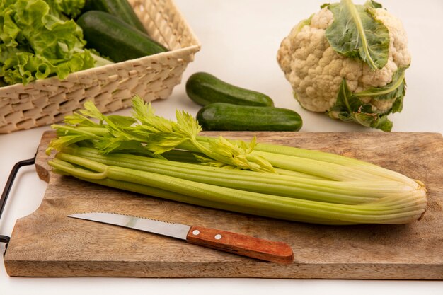 Bovenaanzicht van selderij op een houten keukenbord met mes met komkommers en bloemkool geïsoleerd op een witte achtergrond