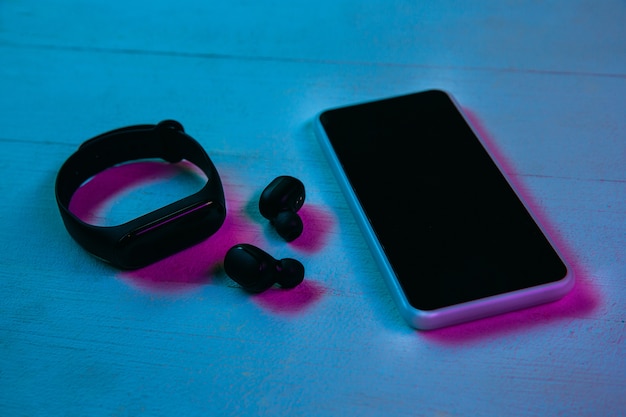 Bovenaanzicht van set gadgets in paars neonlicht en blauwe achtergrond. Smartphone, smartwatch en draadloze koptelefoon op houten tafel. Copyspace voor uw reclame. Tech, modern, gadgets.