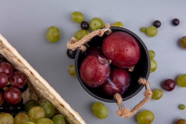 Bovenaanzicht van smaak koning pluots in kom met druiven in mand en druiven bessen op grijze achtergrond