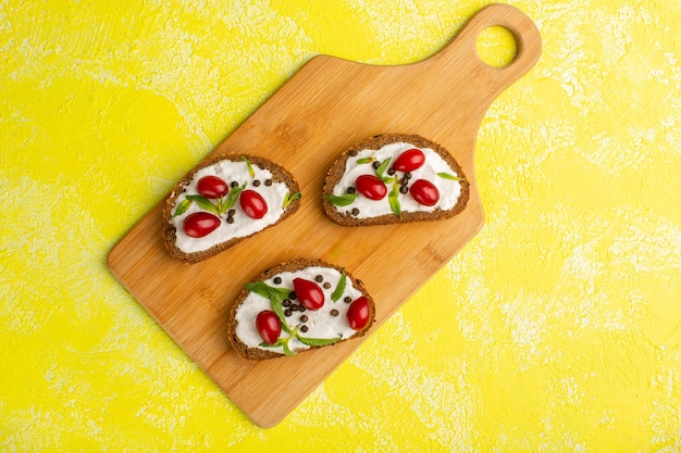 Gratis foto bovenaanzicht van smakelijke brood toast met zure room en kornoeljes op het gele oppervlak