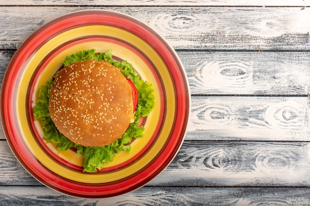 Bovenaanzicht van smakelijke broodje kip met groene salade en groenten binnen gekleurde plaat op rustiek grijs oppervlak