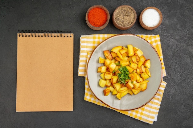 Bovenaanzicht van smakelijke gebakken aardappelen in plaat met kruiden op het donkere oppervlak