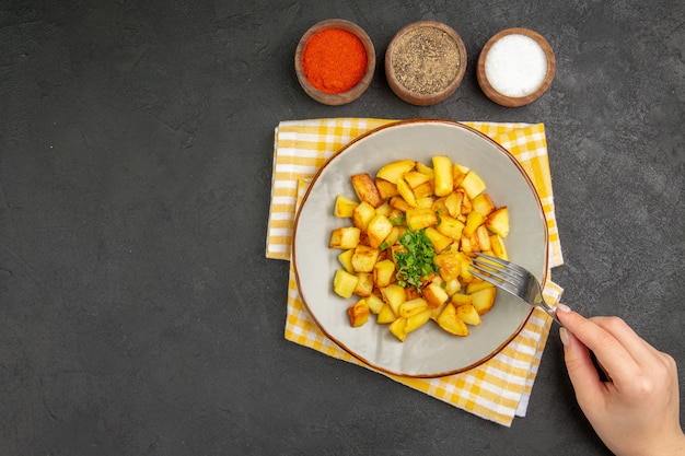 Bovenaanzicht van smakelijke gebakken aardappelen in plaat met kruiden op het donkere oppervlak