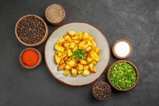 Bovenaanzicht van smakelijke gebakken aardappelen in plaat met kruiden op het donkere oppervlak