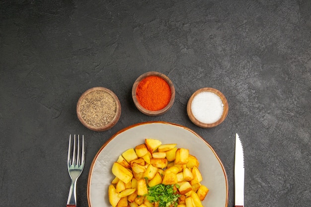 Gratis foto bovenaanzicht van smakelijke gebakken aardappelen in plaat met kruiden op het donkere oppervlak