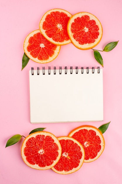 Gratis foto bovenaanzicht van smakelijke grapefruits met kladblok op roze oppervlak