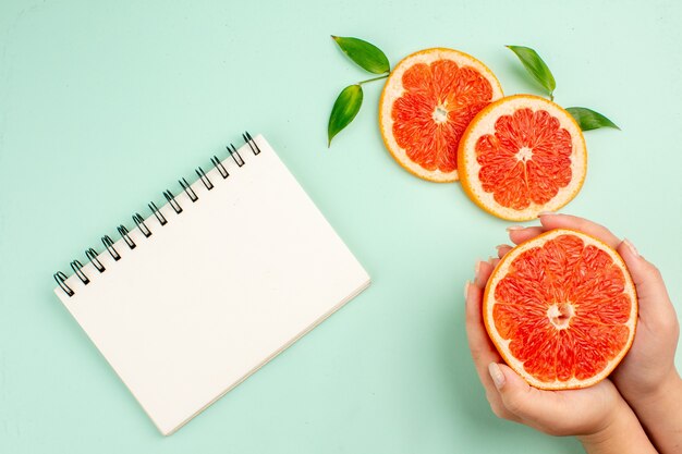 Bovenaanzicht van smakelijke grapefruits sappig gesneden met Kladblok op lichtblauw oppervlak