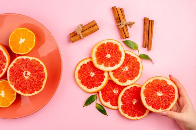 Bovenaanzicht van smakelijke grapefruits sappige fruit plakjes met kaneel op roze oppervlak