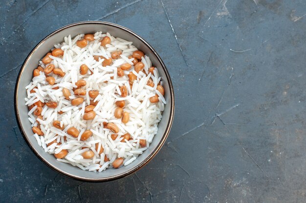 Bovenaanzicht van smakelijke rijstmaaltijd met bonen in een bruine kleine pot op blauwe achtergrond