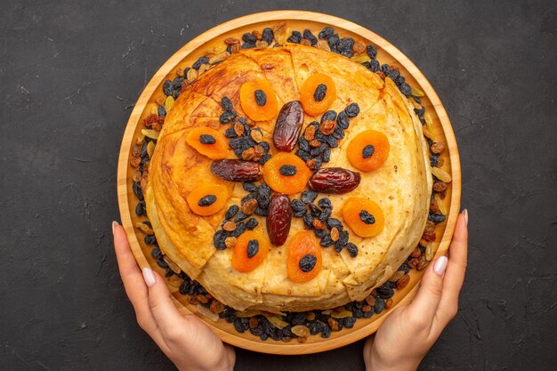 Bovenaanzicht van smakelijke shakh plov gekookte rijst binnen rond deeg met rozijnen op grijze ondergrond