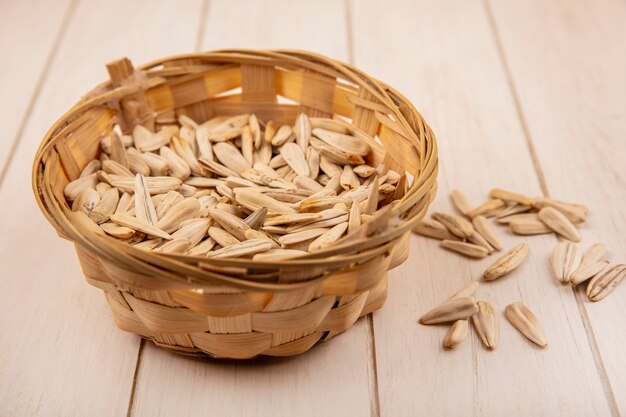 Bovenaanzicht van smakelijke zoute witte zonnebloempitten op een emmer op een beige houten tafel