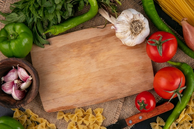 Bovenaanzicht van snijplank met tomaten knoflook bell en hete pepers en uien met munt op een beige servet