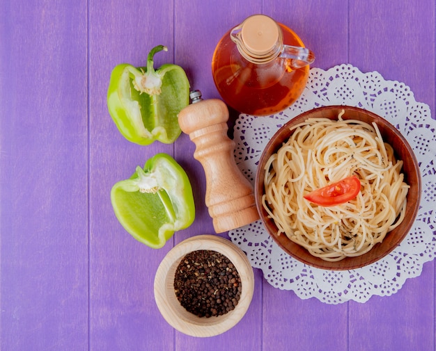 Bovenaanzicht van spaghetti pasta in kom op papier kleedje met half gesneden peper boter zout en zwarte peper op paarse tafel