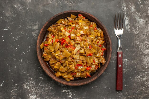 Bovenaanzicht van sperziebonen, tomaten en sperziebonen in de kom naast de vork op de donkere tafel