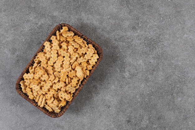 Bovenaanzicht van stapel kleine koekjes in mand over grijze tafel.