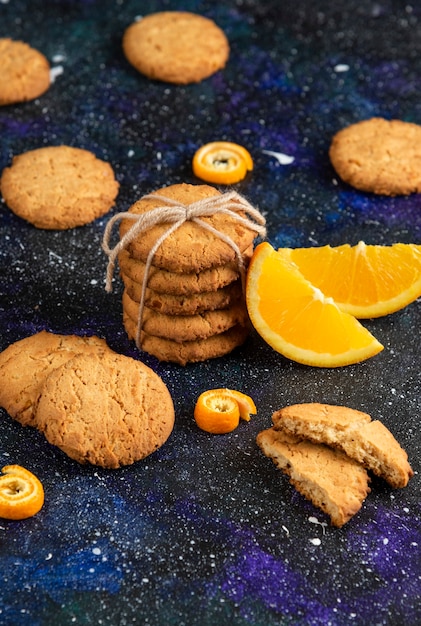 Bovenaanzicht van stapel zelfgemaakte koekjes met sinaasappelschijfje over donkere tafel.