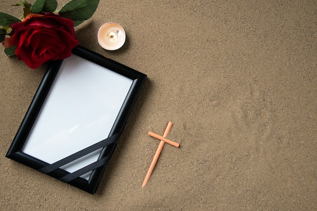 Gratis foto bovenaanzicht van stokkruis met rode bloem en afbeeldingsframe op het zand