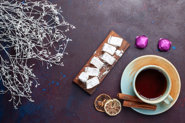 Bovenaanzicht van suiker poedersuiker snoepjes heerlijke nougat met kopje thee op het donkere oppervlak