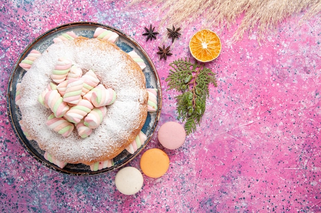 Bovenaanzicht van suiker poedervormige cake met zoete marshmallows en macarons op roze oppervlak