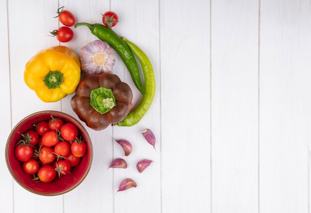 Bovenaanzicht van tomaten in kom en paprika met knoflook op houten oppervlak