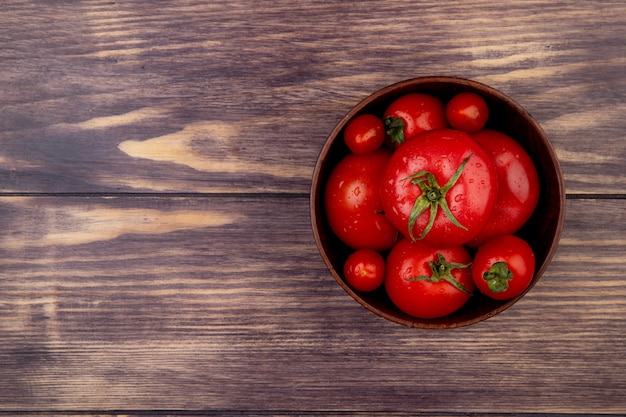 Bovenaanzicht van tomaten in kom op rechterkant en houten oppervlak met kopie ruimte