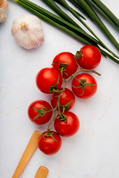 Bovenaanzicht van tomaten met knoflook en lente-uitjes op witte ondergrond