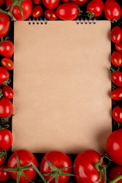 Bovenaanzicht van tomaten rond notitieblok op zwarte ondergrond met kopie ruimte
