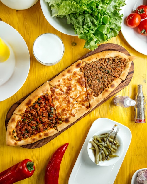 Bovenaanzicht van traditionele turkse keuken turkse pizza pita pide met een andere vulling vleeskaas plakjes kalfsvlees en groenten op een houten tafel