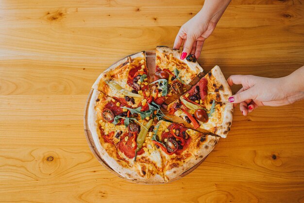 Bovenaanzicht van twee vrouwelijke handen die plakjes van de hele pizza nemen