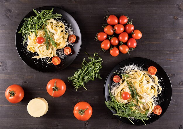 Bovenaanzicht van twee zwarte borden met tagliatelle pasta op houten tafel