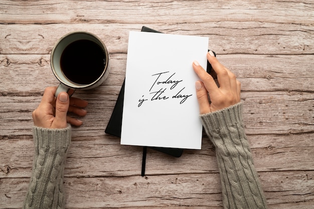 Gratis foto bovenaanzicht van vandaag is het inspirerende citaat van de dag op papier met een vrouw die koffie vasthoudt