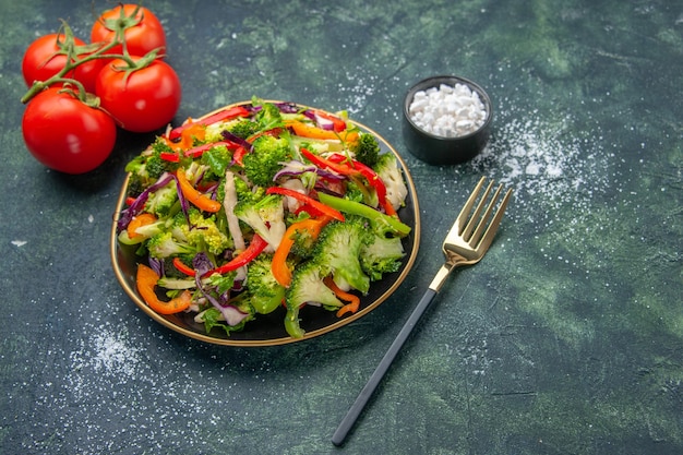 Bovenaanzicht van veganistische salade in een bord met verschillende groenten en vorktomaten met stengel op donkere achtergrond