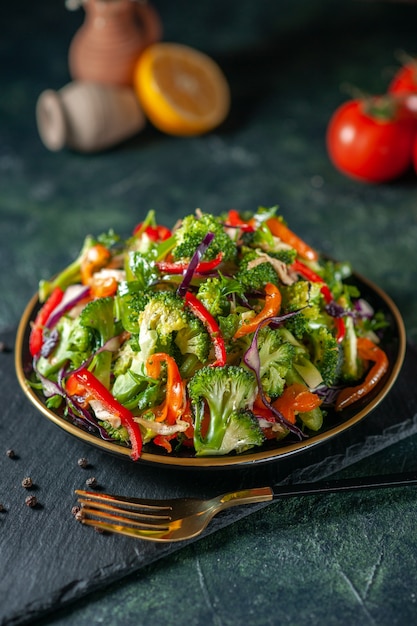 Bovenaanzicht van veganistische salade met verse ingrediënten in een bord en peper op zwarte snijplank