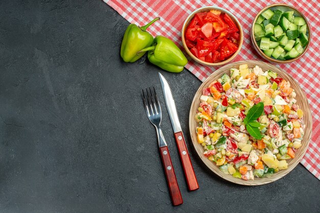 Bovenaanzicht van vegetarische salade in kom met rode servet eronder en bestek met groenten aan de zijkant en plaats voor tekst op donkergrijze achtergrond