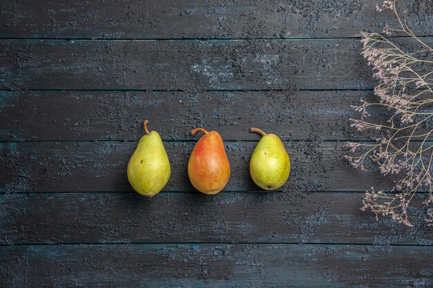 Bovenaanzicht van ver groen-geel-rode peren twee groene peren en een rood-gele peer in het midden van grijze tafel naast de boomtakken