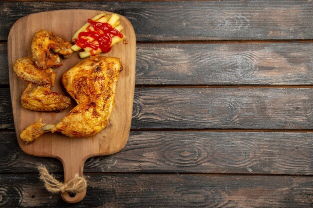 Bovenaanzicht van veraf kip smakelijke frietjes kip en ketchup op de houten snijplank aan de linkerkant van de donkere tafel