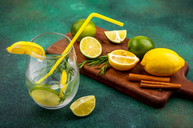 Bovenaanzicht van verfrissend detox water in een glas met citroenen en limoen op een houten keuken bord met kaneelstokjes op groene ondergrond