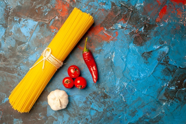 Bovenaanzicht van vermicelli pasta's vastgebonden met touw en tomaten peper knoflook aan de rechterkant op blauwe achtergrond