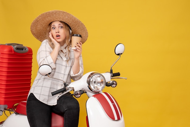 Bovenaanzicht van verrast jonge vrouw hoed dragen en zittend op de motorfiets en koffie te houden