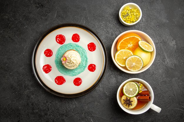 Bovenaanzicht van verre bessen en chocoladeplaat met cupcake met witte room en sauzen naast de kommen met kruiden en gesneden citroenen en kopje thee