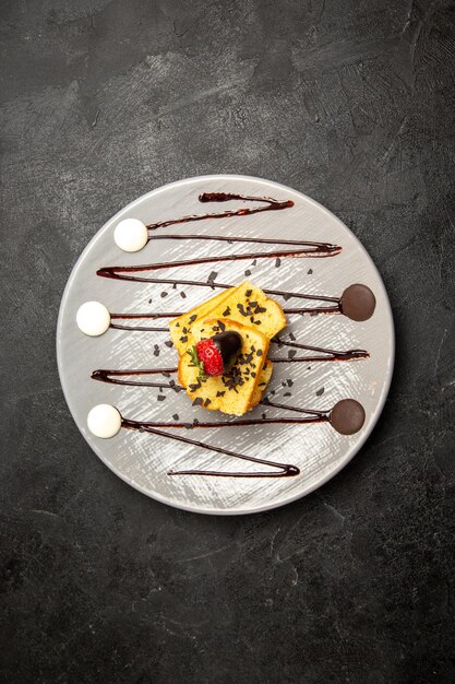 Bovenaanzicht van verre cake smakelijke cake met met chocolade omhulde aardbeien en chocoladesaus op de grijze plaat op de donkere tafel