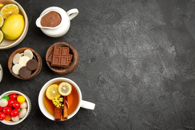 Bovenaanzicht van verre chocolade en citroenchocoladeroomsnoepjes en citroenen in kommen naast het kopje kruidenthee op de donkere tafel