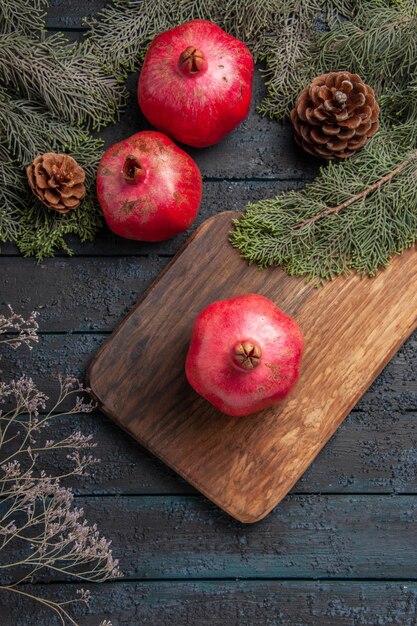 Bovenaanzicht van verre granaatappels en kegels smakelijke granaatappel op snijplank naast twee granaatappels en takken met kegels op grijs oppervlak