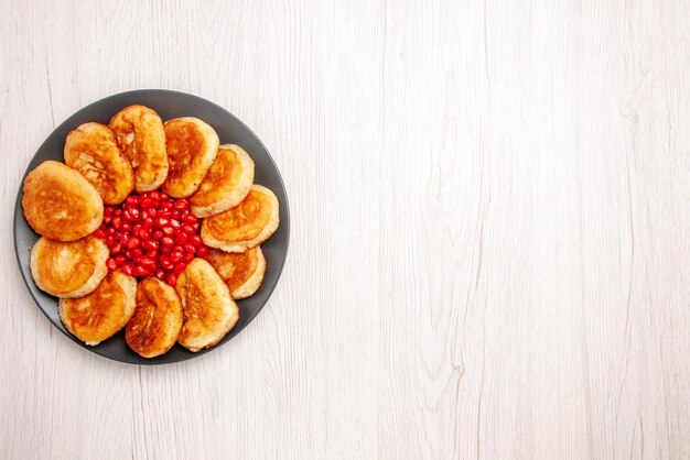 Bovenaanzicht van verre pannenkoeken smakelijke pannenkoeken met granaatappel op de zwarte plaat aan de linkerkant van de witte tafel