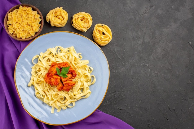 Bovenaanzicht van verre pasta en vleeskommen met pasta en bord met pastajus en vlees op het paarse tafelkleed