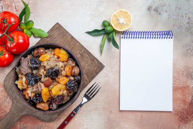 Bovenaanzicht van verre pilaf de snijplank met pilaf vork tomaten citroen witte notebook